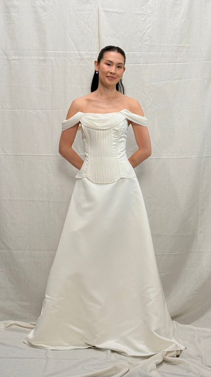 Woman wearing a white off-shoulder gown against a plain background