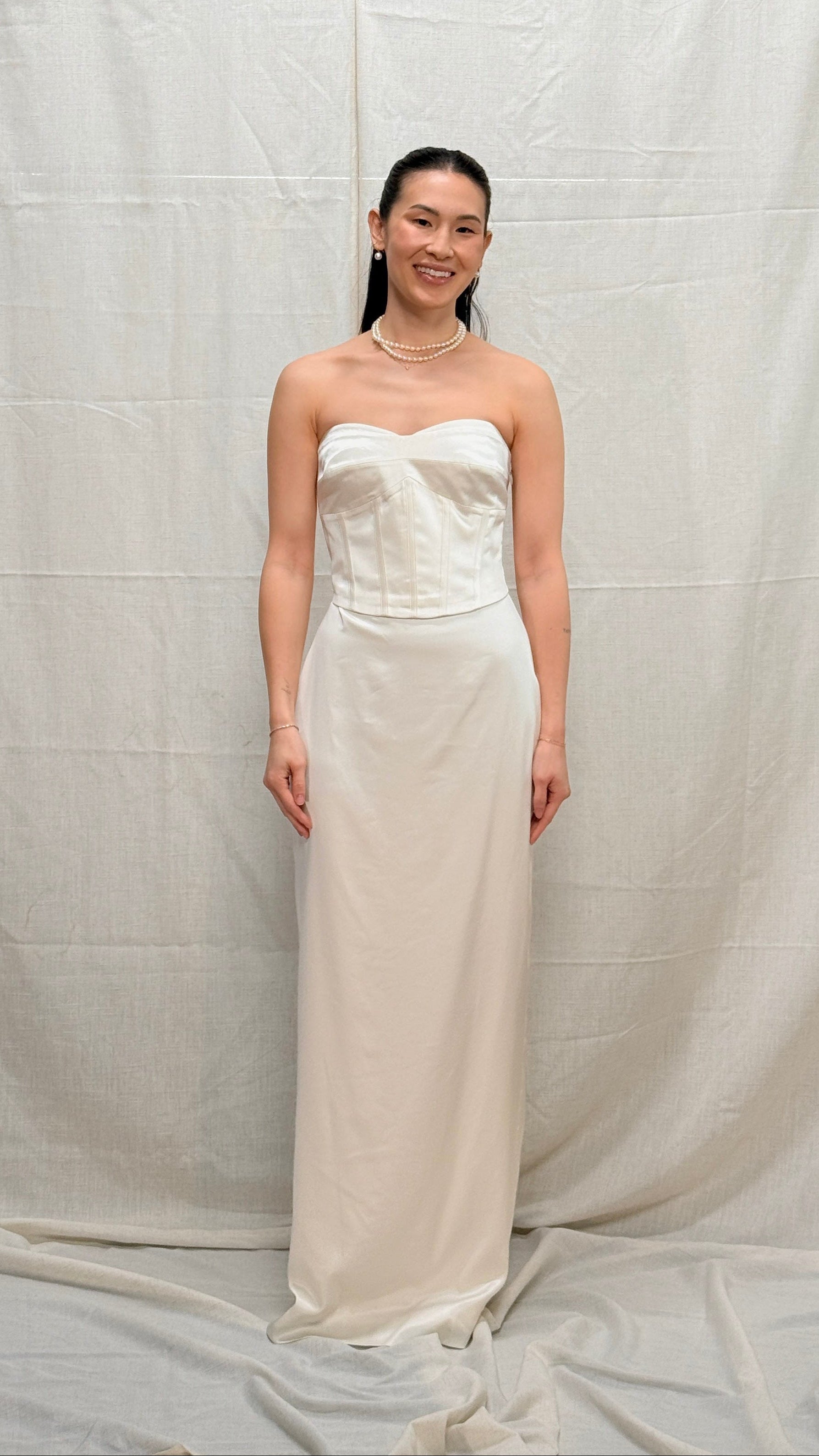 Woman wearing a strapless white gown against a plain background