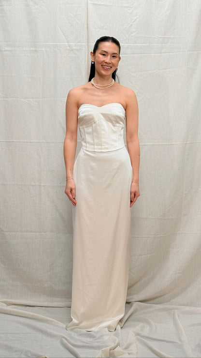 Woman wearing a strapless white gown against a plain background